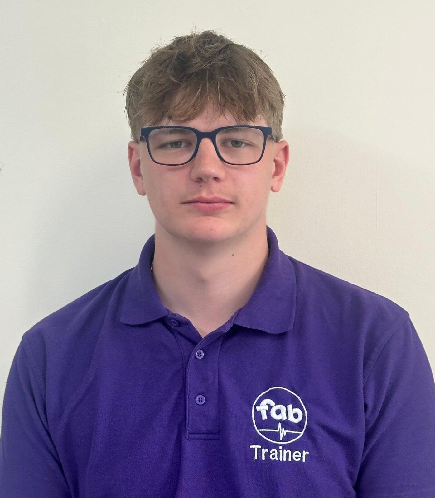 FabTraining team member and certified first aid instructor wearing branded purple polo shirt, with short light brown hair and glasses